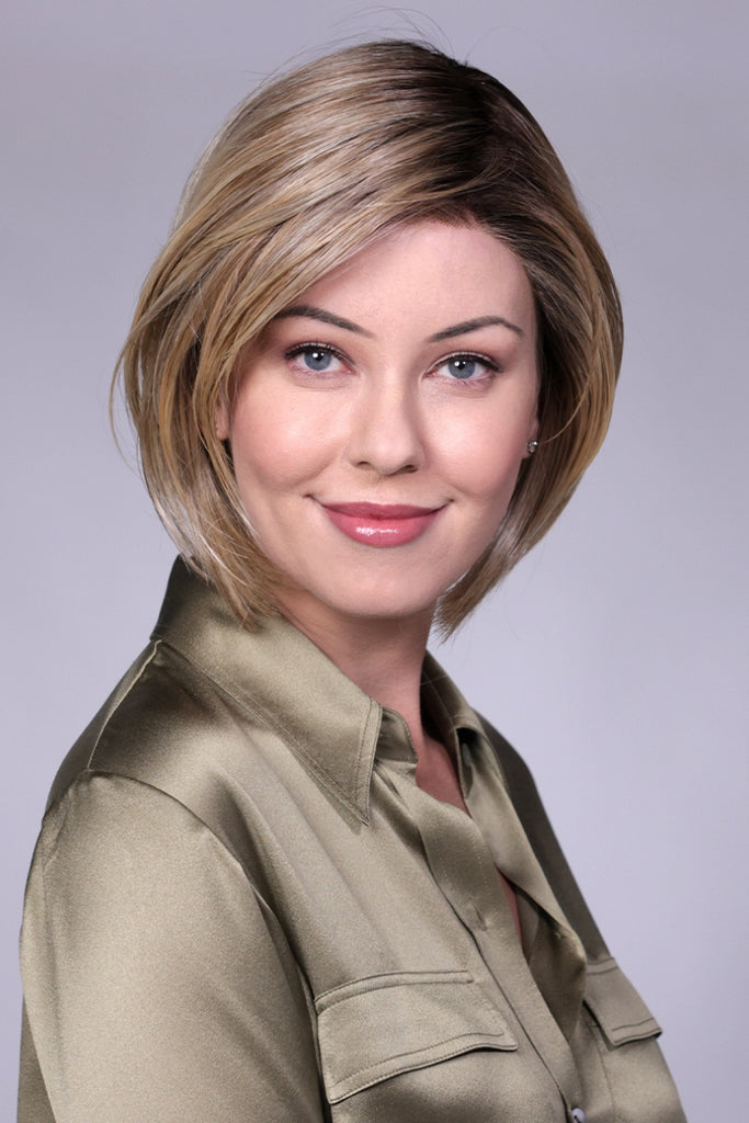 Front view of model styling a dark rooted medium brown wig with stone blonde and caramel blonde highlights.