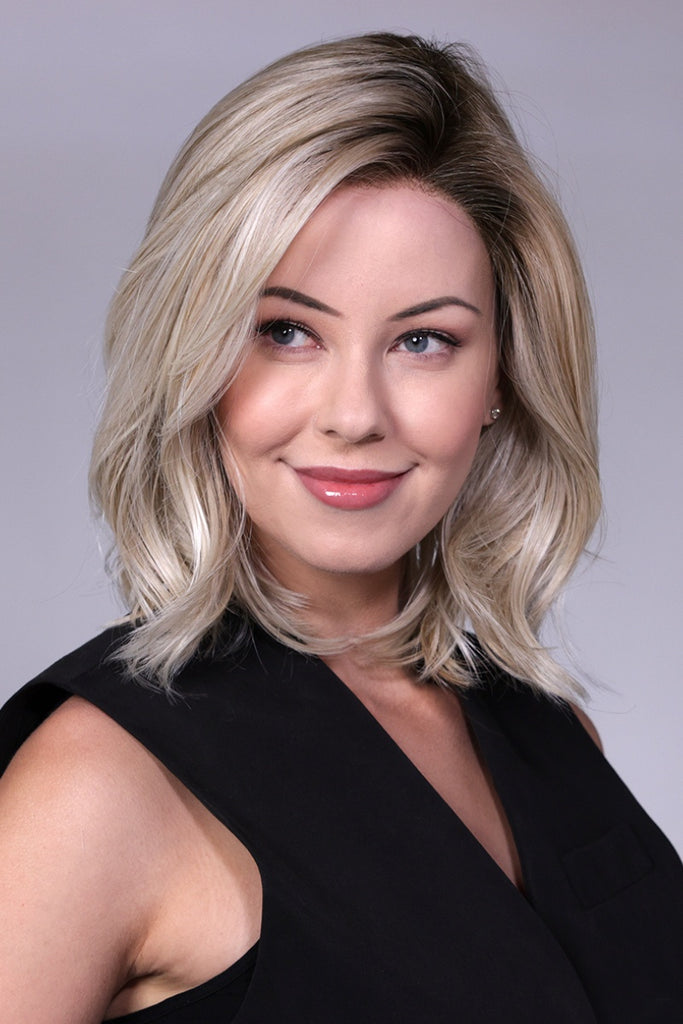 Model wearing a platinum blonde wig with light brown lowlights and a dark brown root.