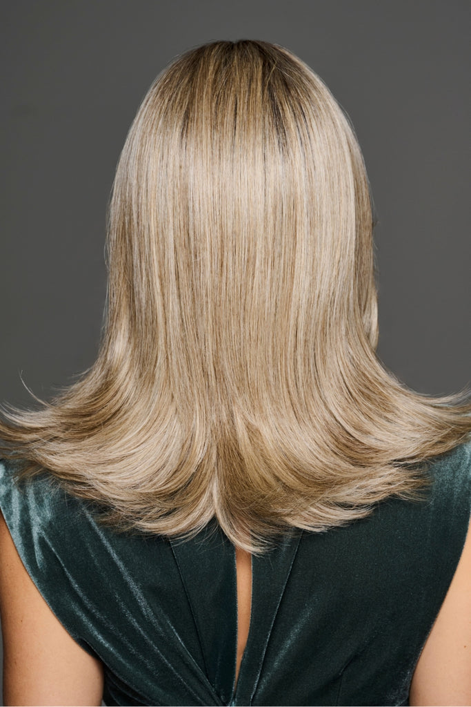 Model styling a wig with a honey blonde base with a dark root and pale blonde woven throughout.