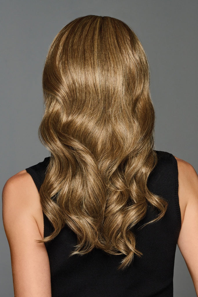 Back view of woman wearing a light golden brown wig with cool blonde highlights and dark brown roots.