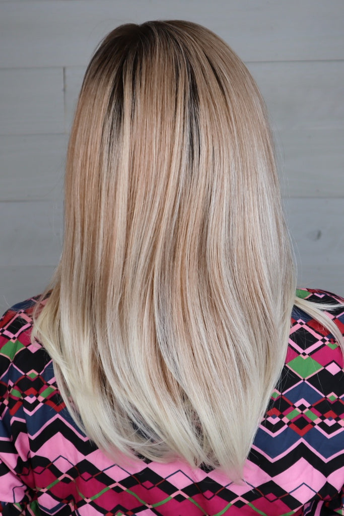 Back profile of model wearing a long blonde wig with dark roots.