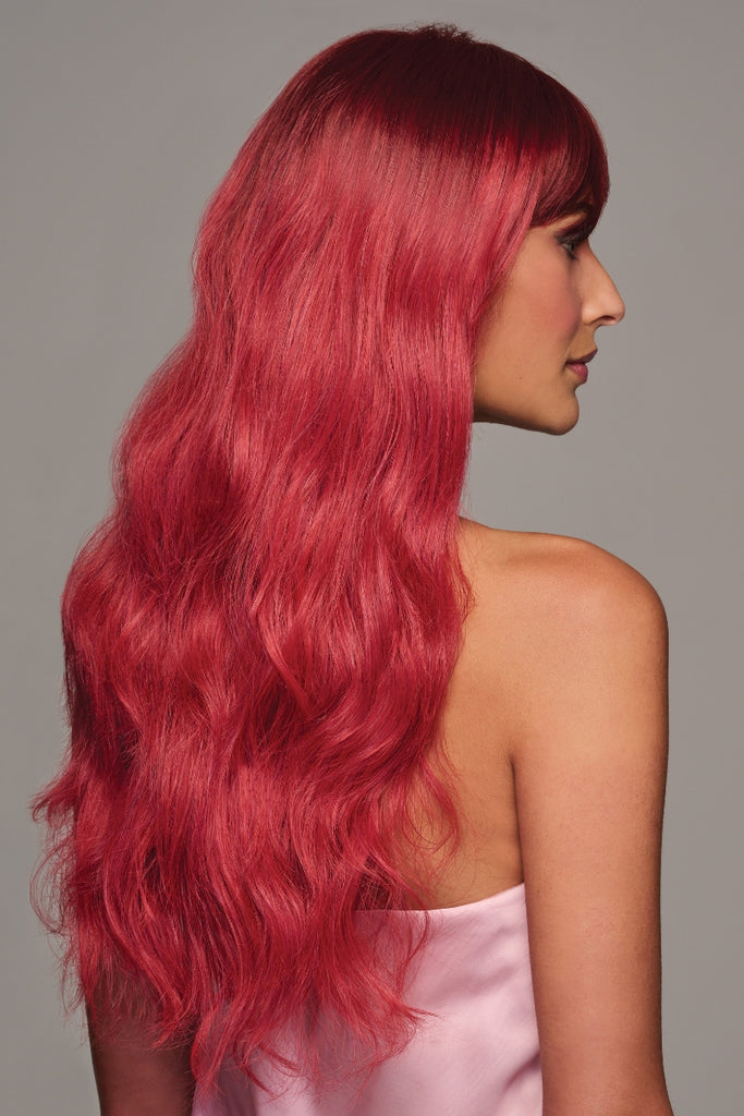 Woman styling a red, wavy wig that falls to her mid-back.