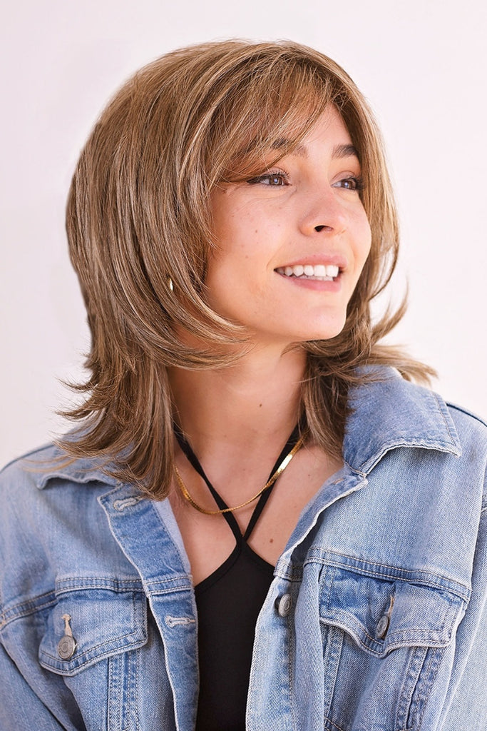 Woman wearing a shaggy medium length wig with curtain bangs.